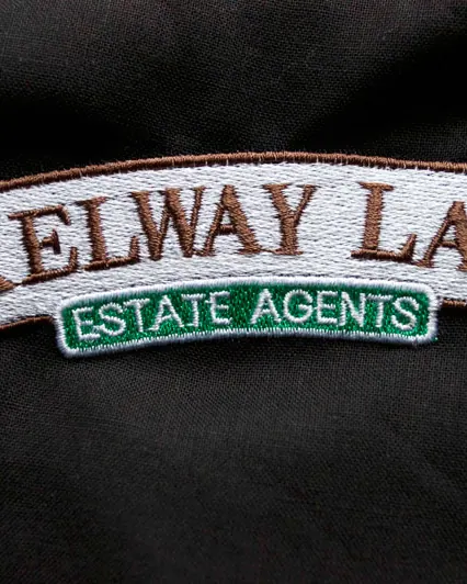 Estate agency name badge embroidered in white on black with a red merrow border.