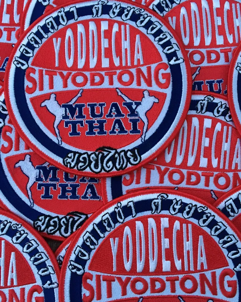 A pile of red and blue embroidered Muay Thai club patches with merrow borders.