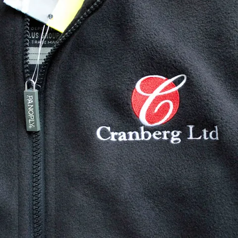 Close-up of a company logo embroidered in red and white on a black fleece jacket.