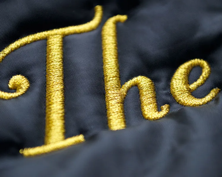 Gold metallic thread script lettering embroidered on black satin.