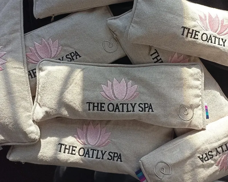 A pile of natural linen eye pillows, each embroidered with a pink lotus and a spa's name.