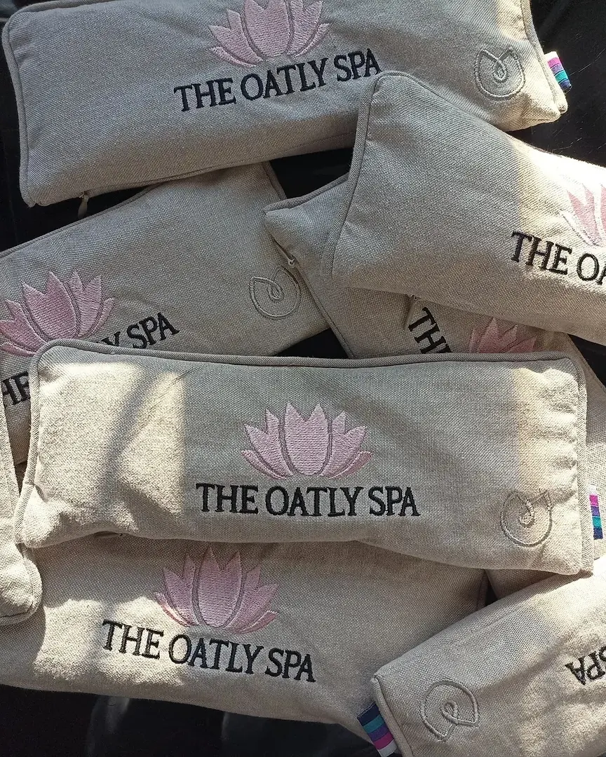 A pile of natural linen eye pillows, each embroidered with a pink lotus and a spa's name.