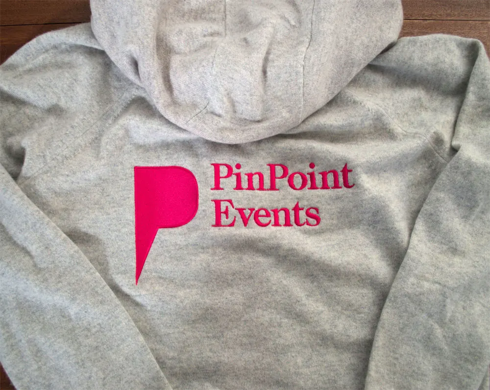 Grey hoodie with a pink events-company logo embroidered on the chest.
