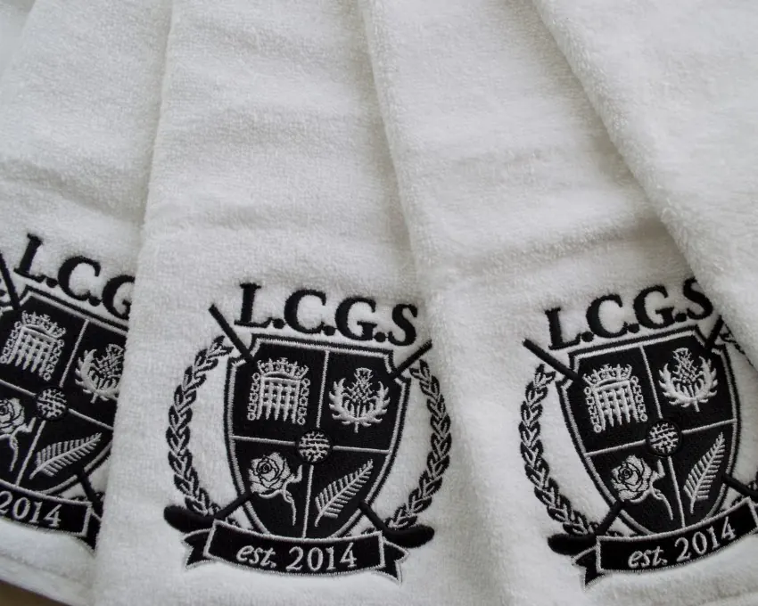 A stack of white polo shirts each embroidered with a school crest.