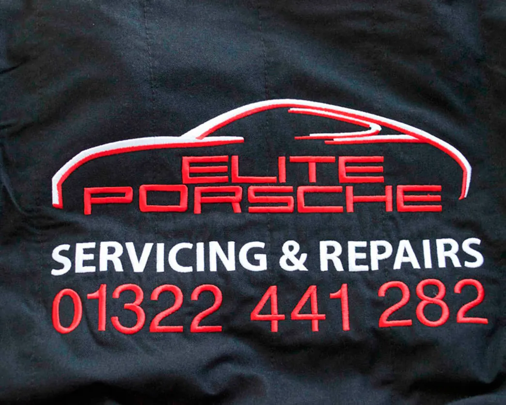 Navy workwear jacket with a red and white garage logo and phone number embroidered on the back.