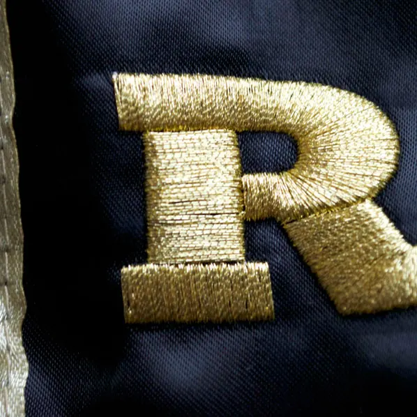 Raised gold metallic thread monogram embroidered on navy fabric.