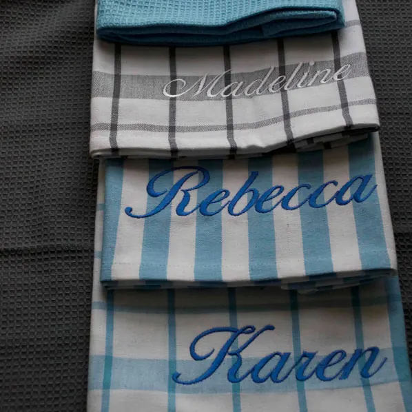 A set of striped cotton tea towels each embroidered with a different name in script.